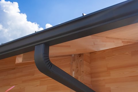 Close-up of a contemporary dark gray rain gutter and downspout system installed on the wooden eaves and exterior wall