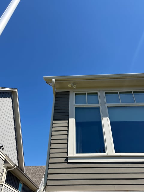 Modern house exterior with gray siding, large white-trimmed windows, and clear blue sky
