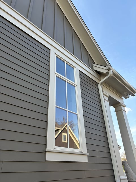 Gray house with white trim window and reflection of another building, clear blue sky visible above