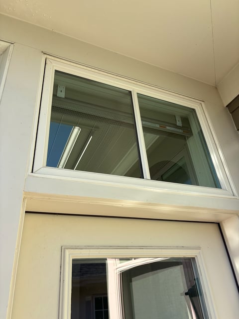 Two rectangular windows stacked vertically on a cream-colored wall with white frames and green-tinted glass panes