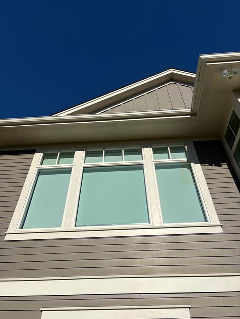Modern house exterior with large multi-pane window, light-colored siding, and pitched roof against clear blue sky