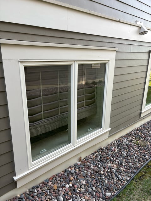 Pair of white-framed glass sliding patio doors on a modern house exterior with gray horizontal siding and gravel landscaping