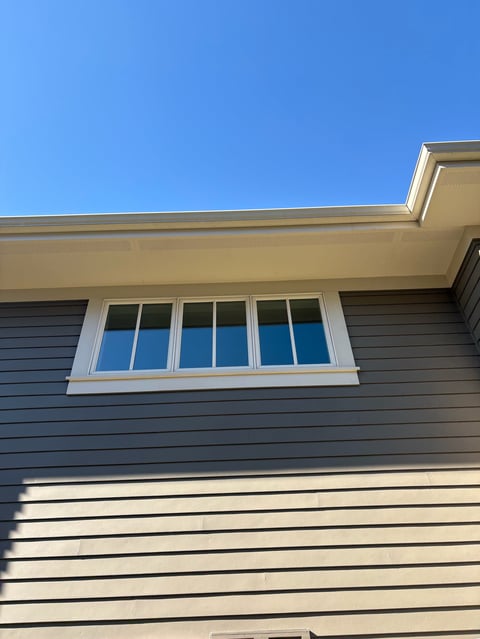 Modern house exterior with dark gray siding, cream trim, and multi-pane window under clear blue sky