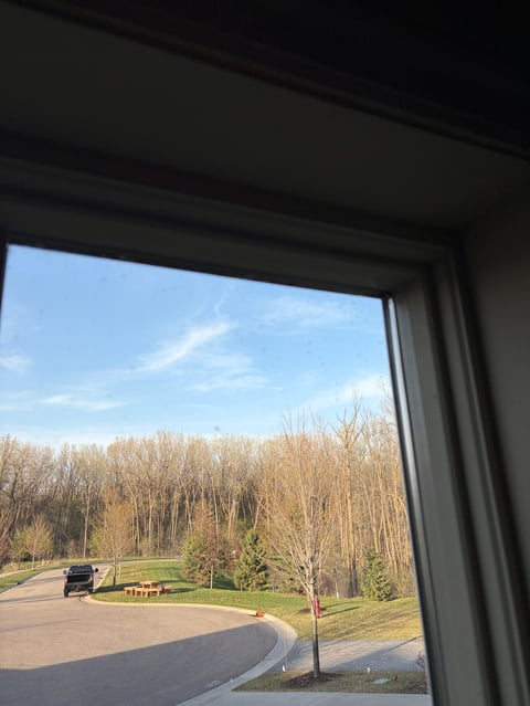 View through a window of a curved driveway with parked vehicle, bare trees, and blue sky beyond