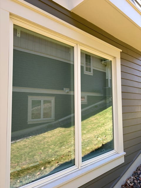 Two large sliding glass doors with cream frames on a beige house exterior, reflecting backyard grass and landscaping